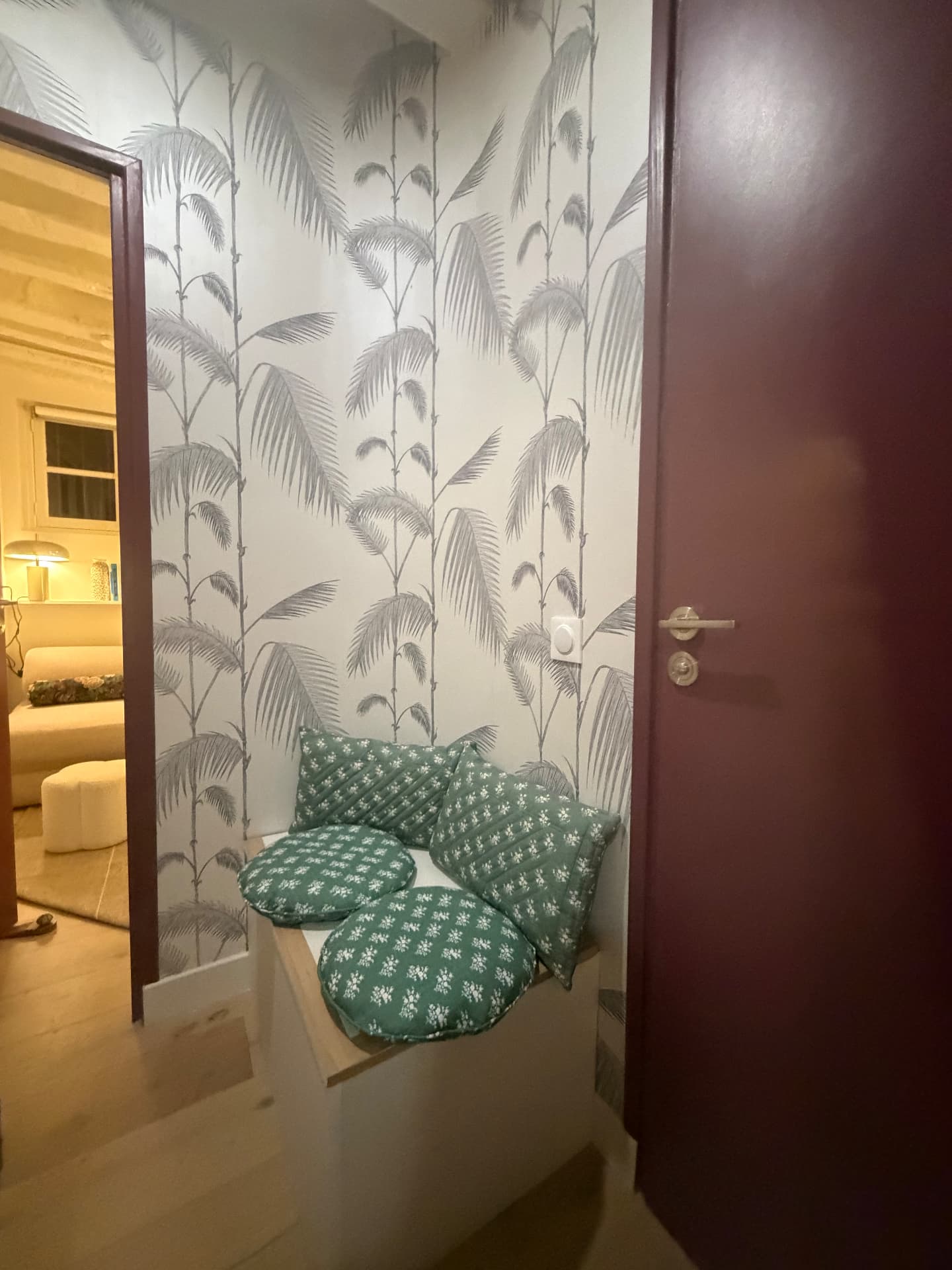 Un recoin du cabinet avec coussins verts et papier peint végétal